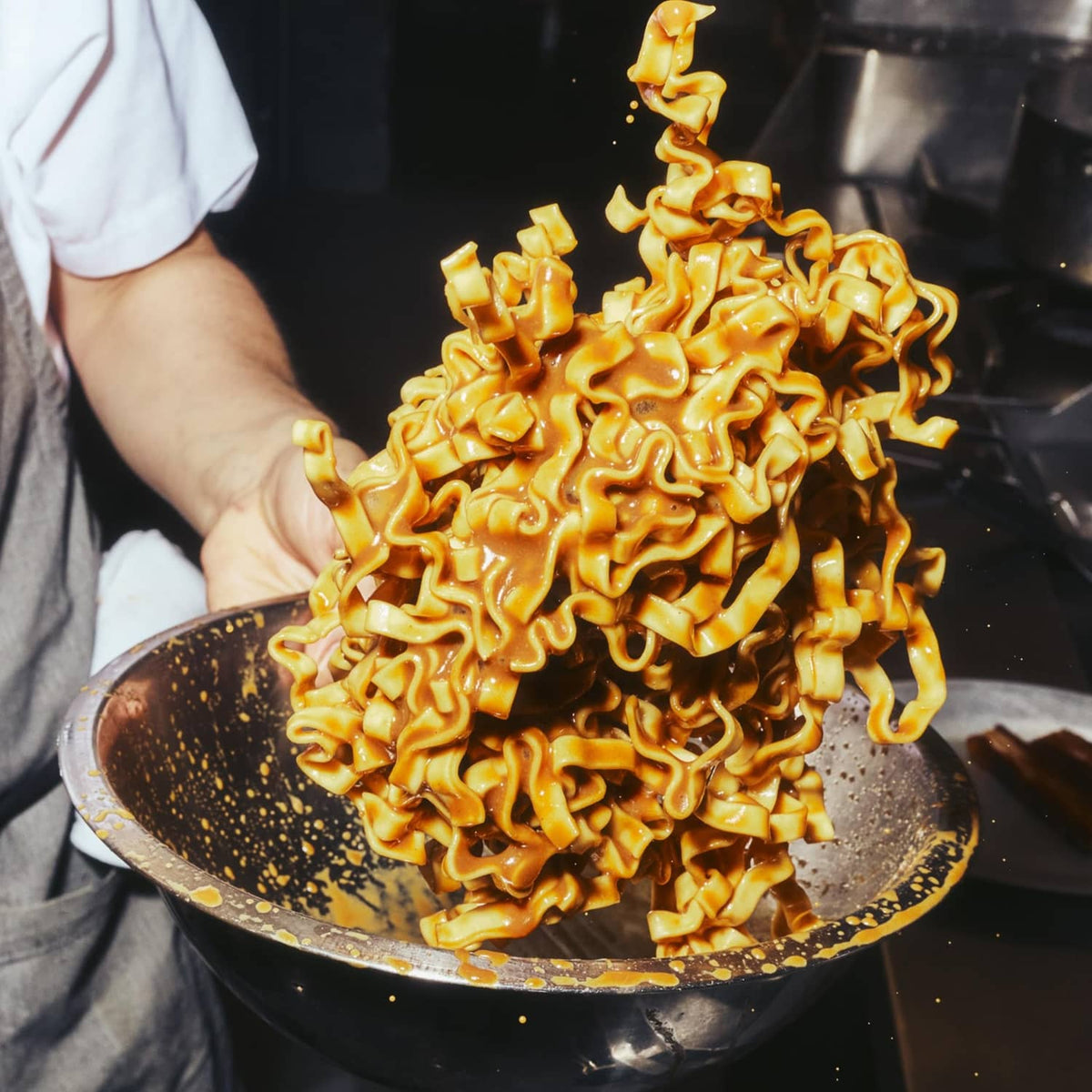 Cooked sesame miso noodles piled in a skillet with chef hand and utensil