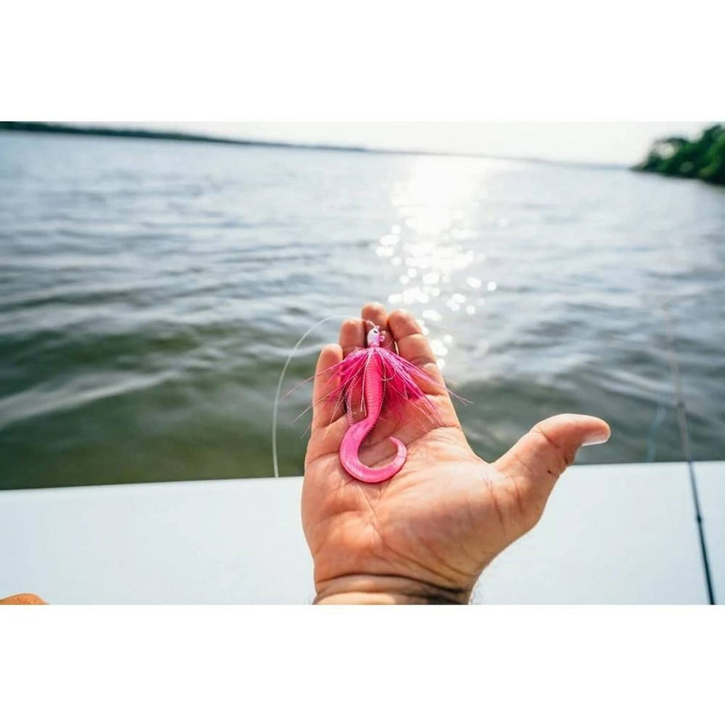 Pink soft fishing bait with curled tail held in hand