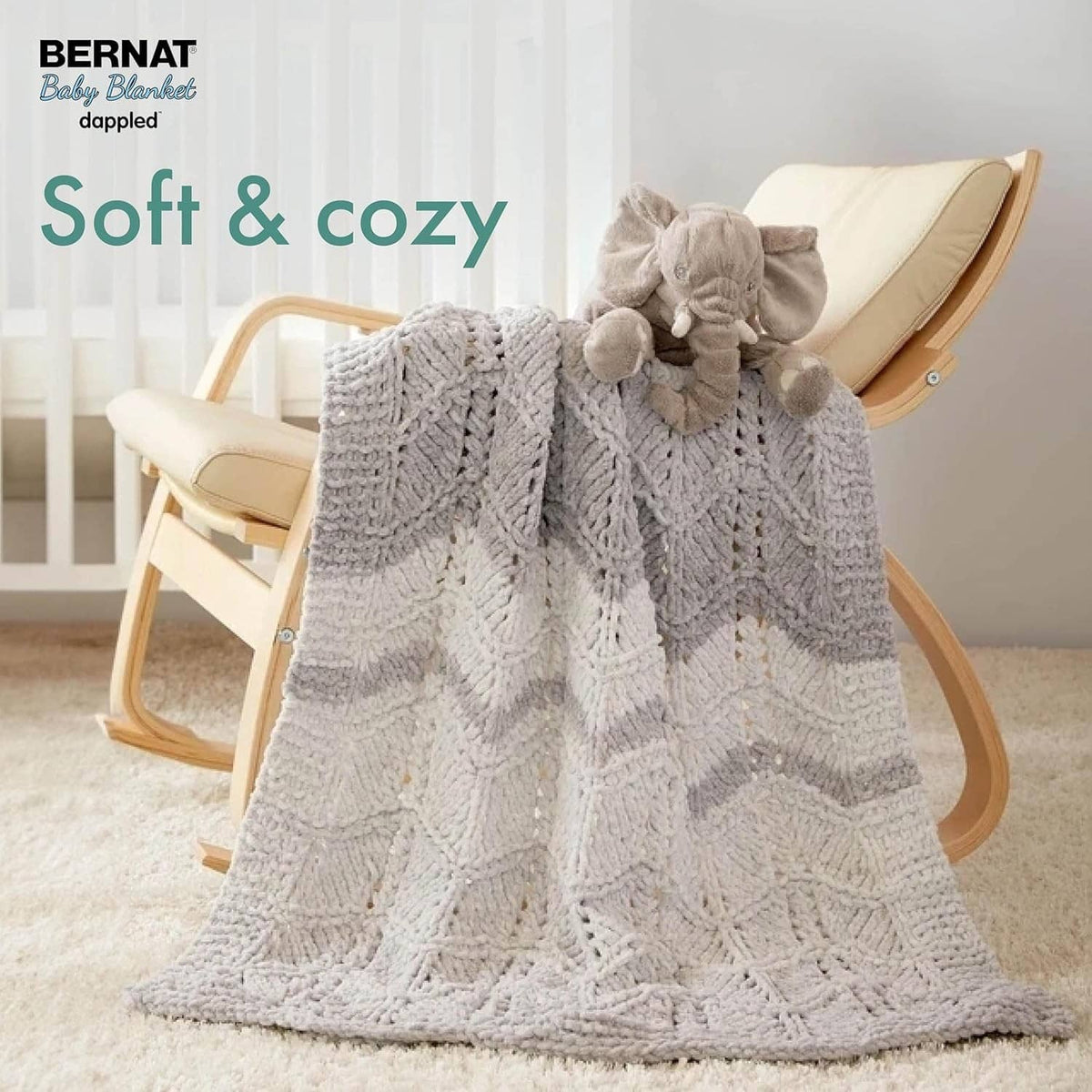 Gray dappled chunky knit baby blanket draped with soft textured pom accents