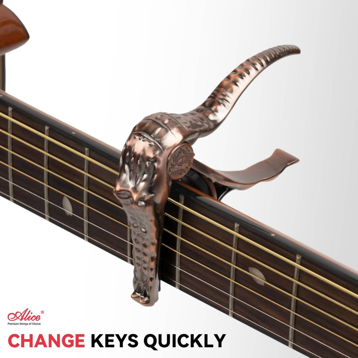 Bronze alligator-style guitar capo clamped on guitar fretboard near sound hole