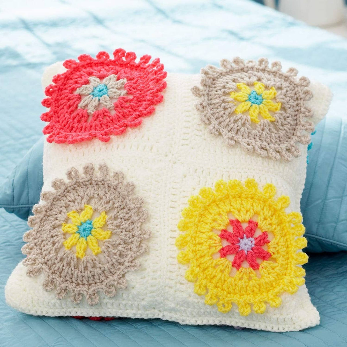 Crocheted square pillow cover with red, beige, and yellow flower appliques