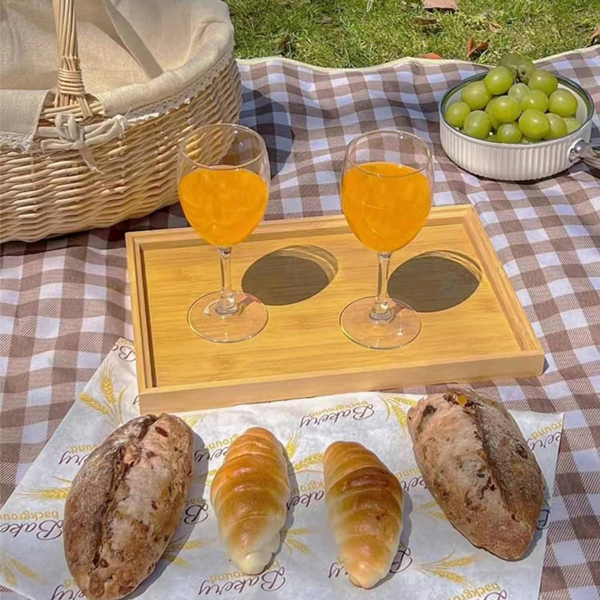 Brown and white checkered picnic blanket with wooden tray and glasses on top