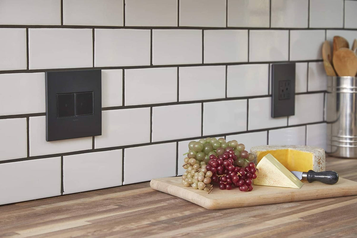 Two graphite 2-gang wall plates on a white subway tile backsplash