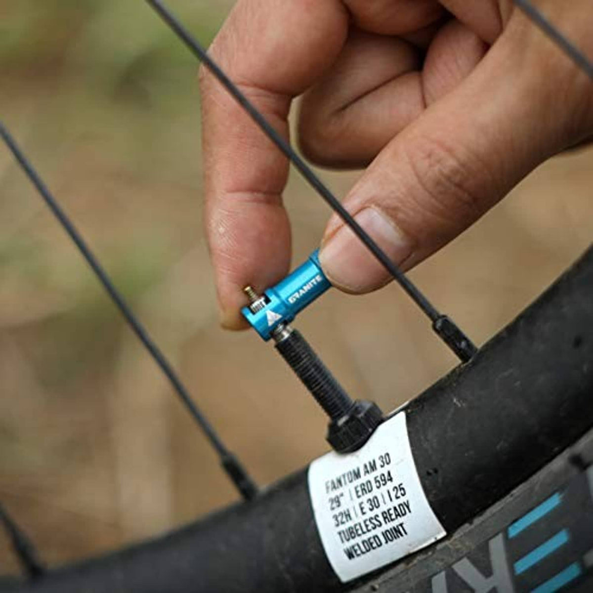 Blue valve core remover cap on a bike tire valve during installation by hand.