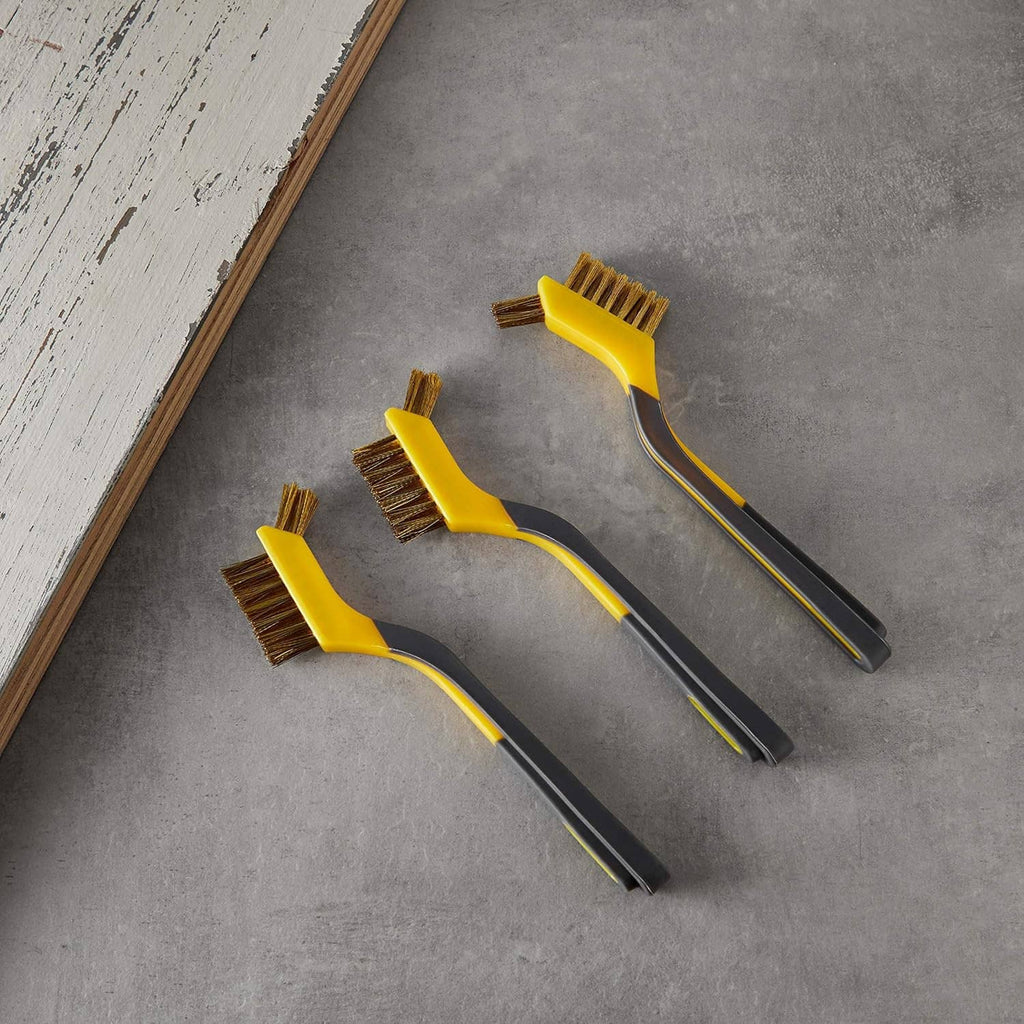 Three mini brass wire brushes with yellow heads on a flat gray surface