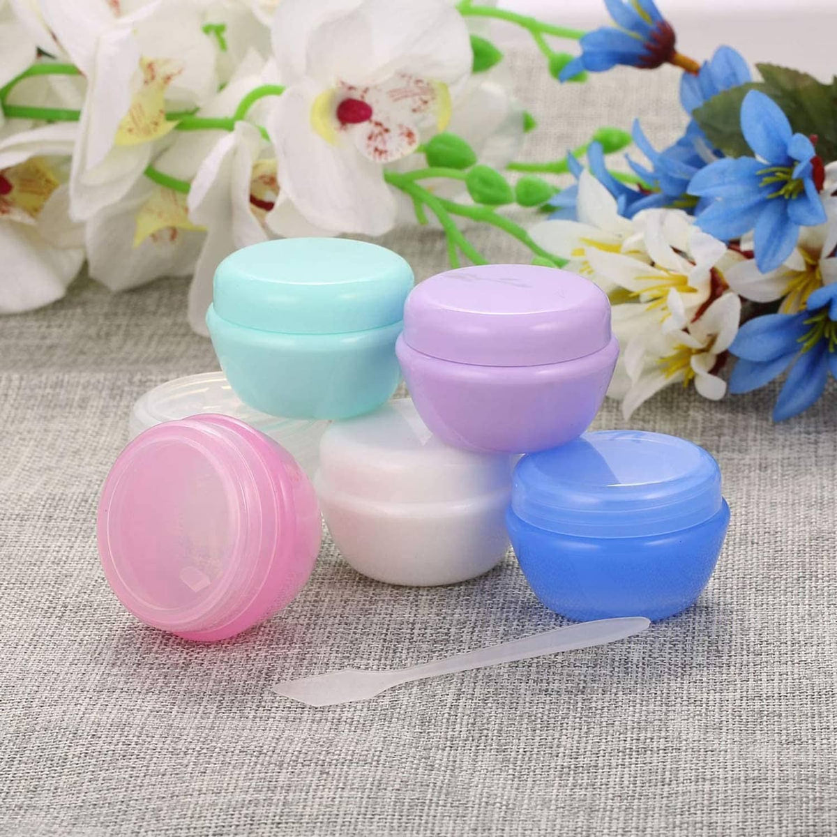 Assorted pastel 1 oz plastic toiletry jars with matching lids arranged on fabric