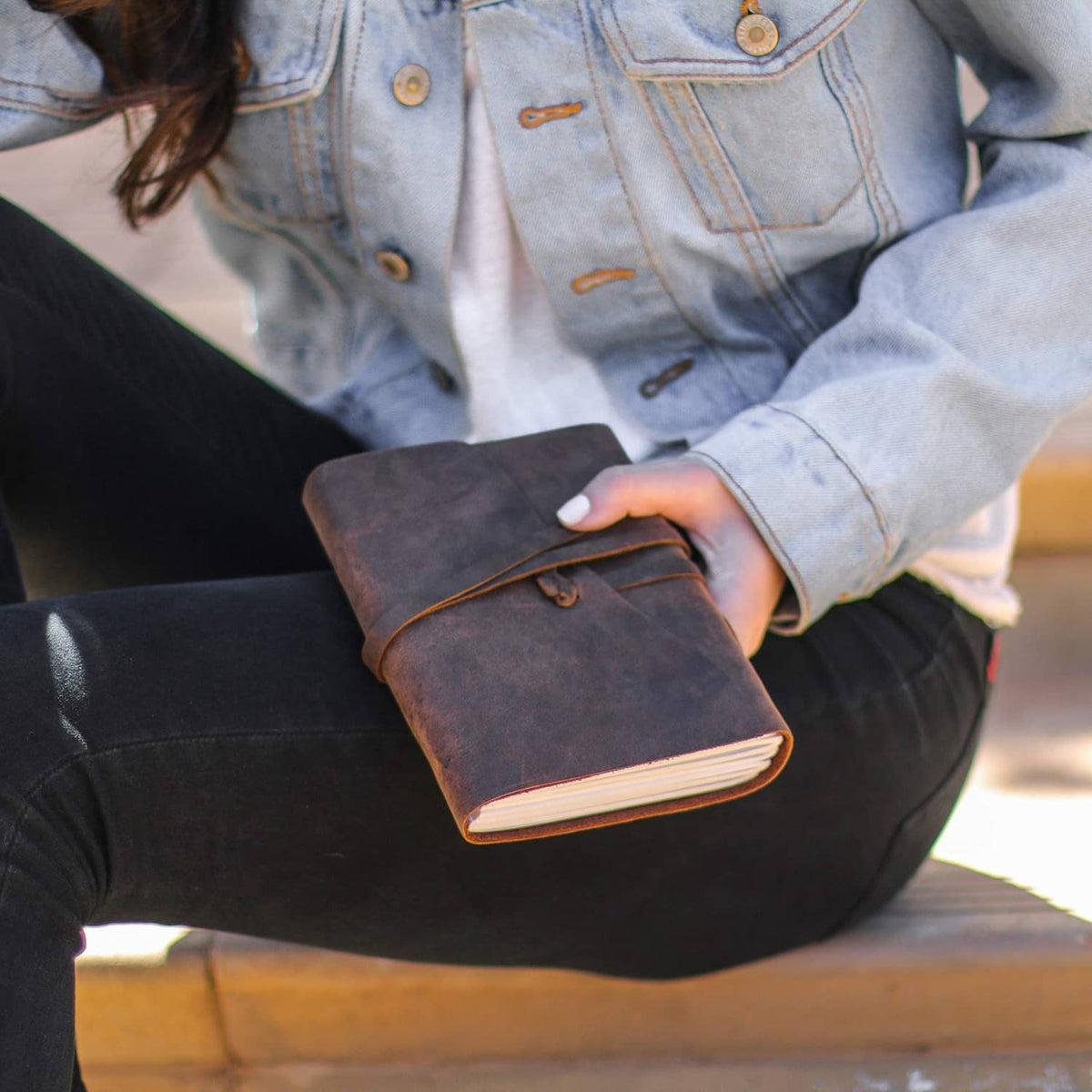 Brown leather journal notebook held closed with wrap strap and stitched edge.