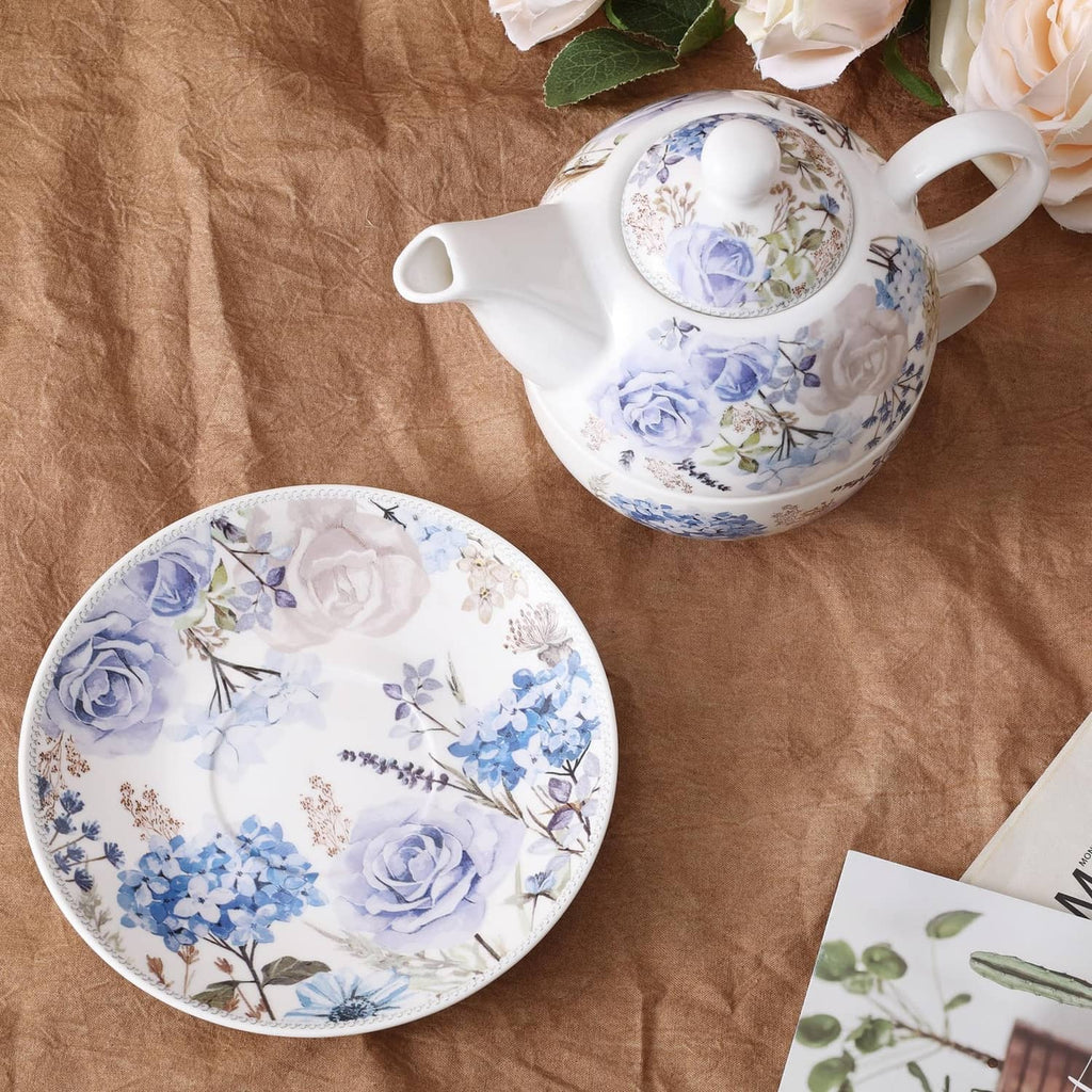 Porcelain teapot and saucer with blue rose floral pattern, flat lay.