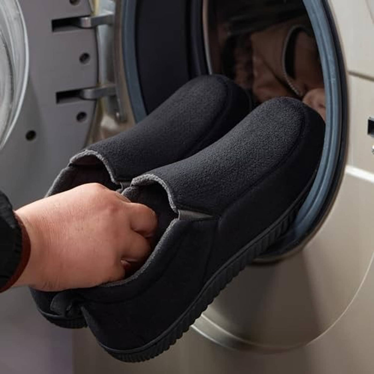 Black closed-back slippers being put on, plush collar and cushioned sole visible.