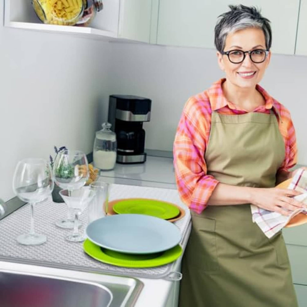 Gray microfiber dish-drying mat on counter near sink; person preparing dishes with mat.