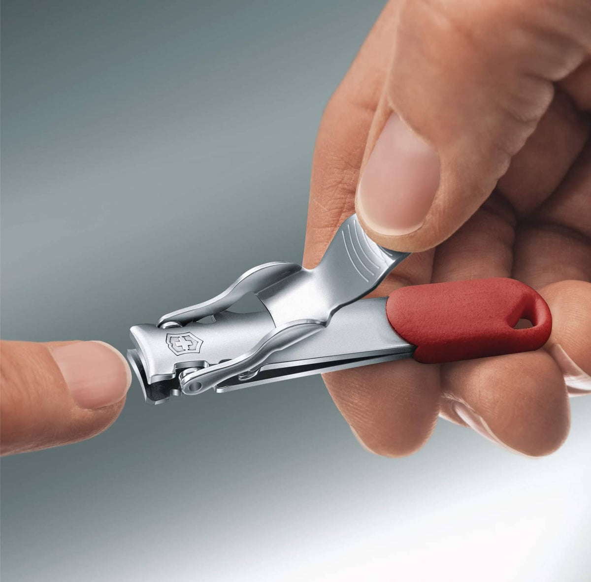 Nail clipper held in hand, red handle and stainless steel head