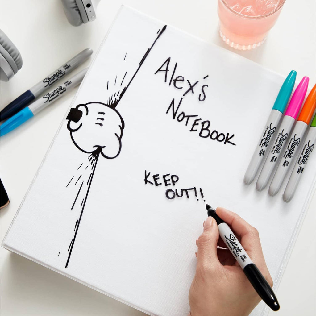 Fine-point permanent marker with dark tip in a hand on an open notebook