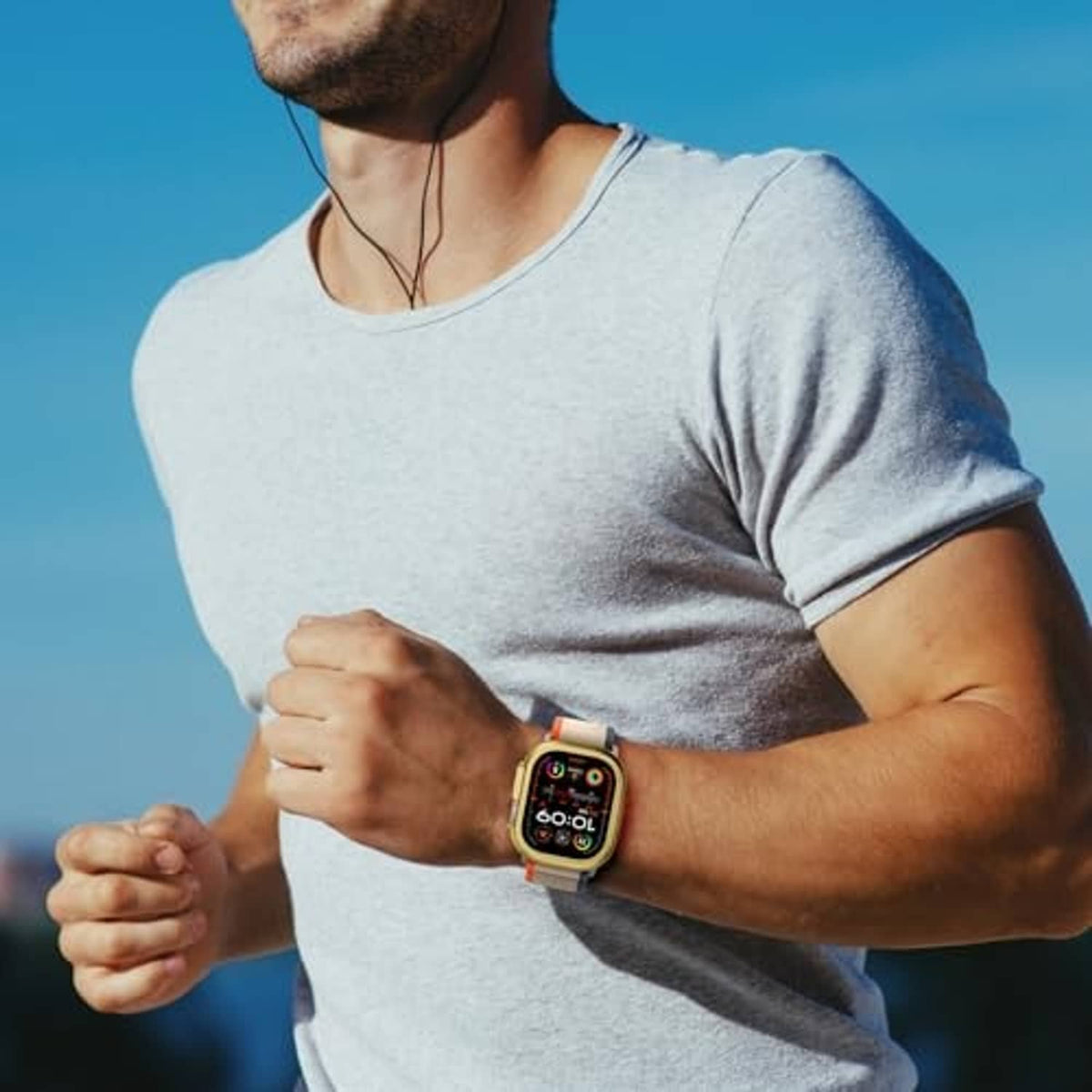 Gold metal watch case on a wrist with a light gray athletic watch strap