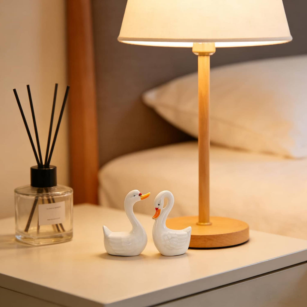 Two small white ceramic swan figurines on a tabletop, facing each other
