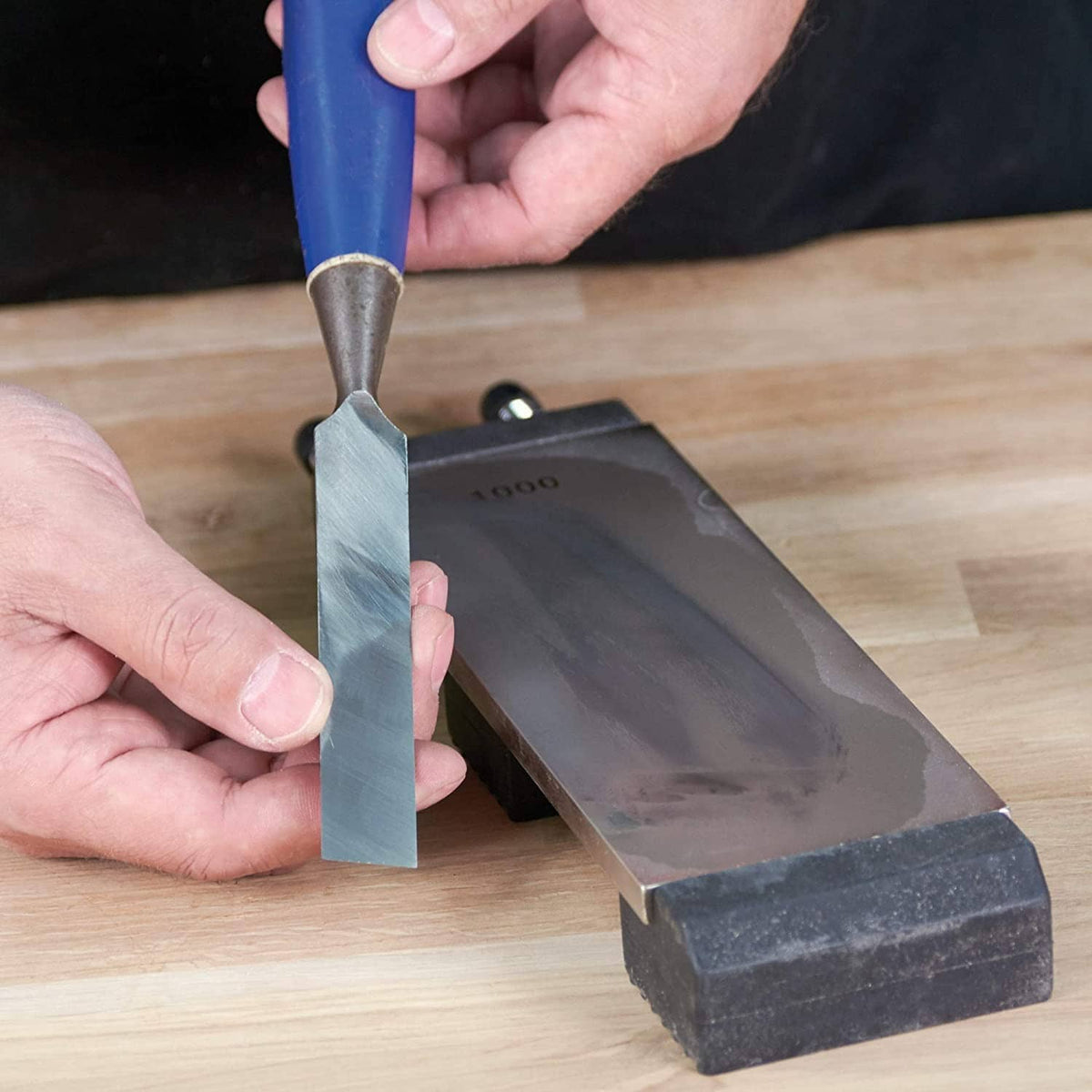 Hands using a flat metal lapping plate on a sharpening surface with abrasive coating