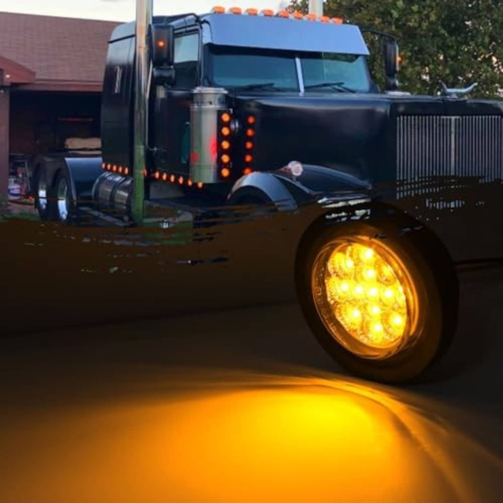 Round amber LED side marker light on a truck, glowing yellow near the front wheel