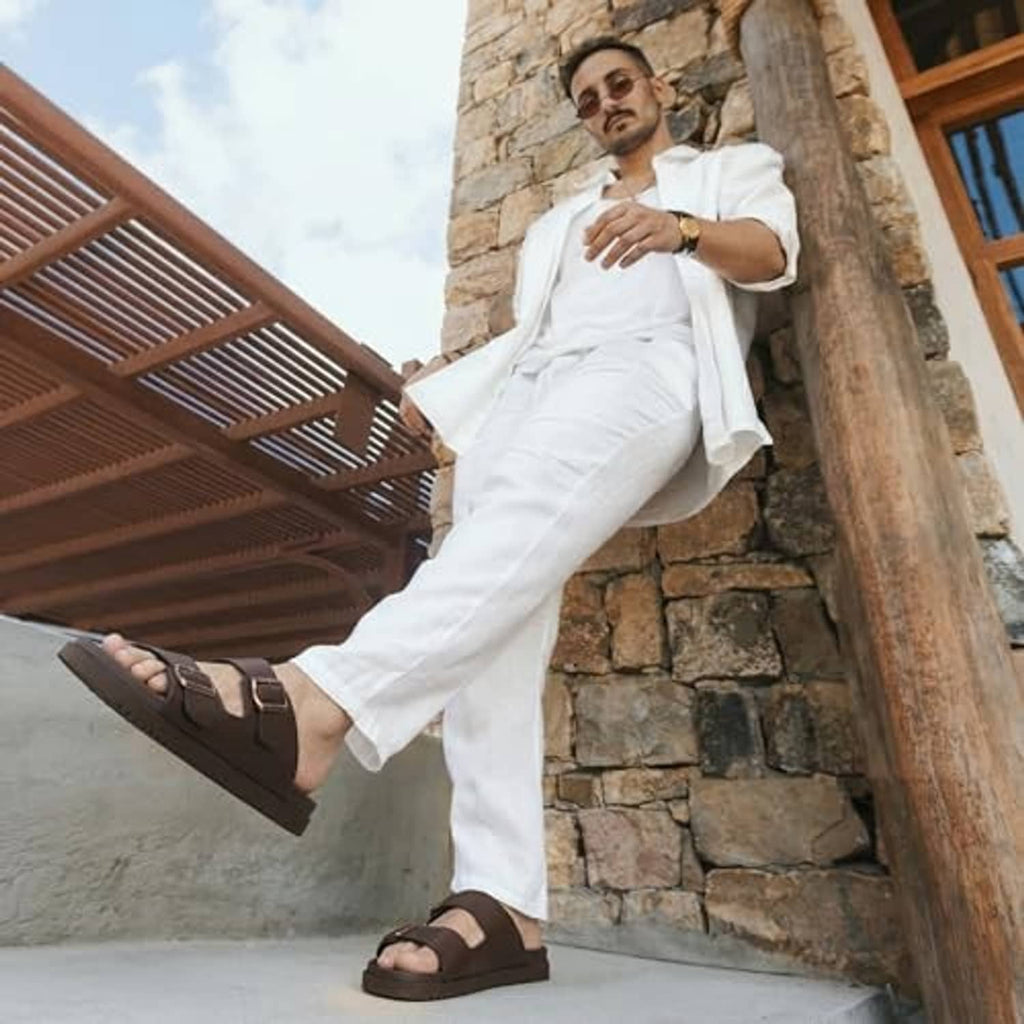 Men's brown buckle slide sandals worn with white pants