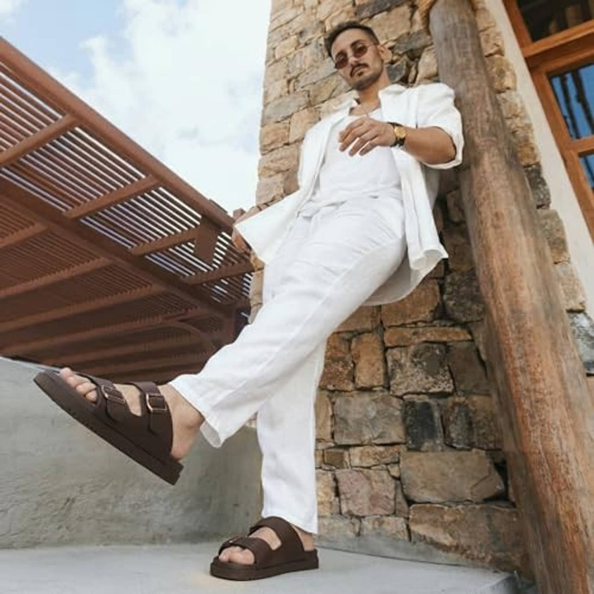 Men's brown buckle slide sandals worn with white pants