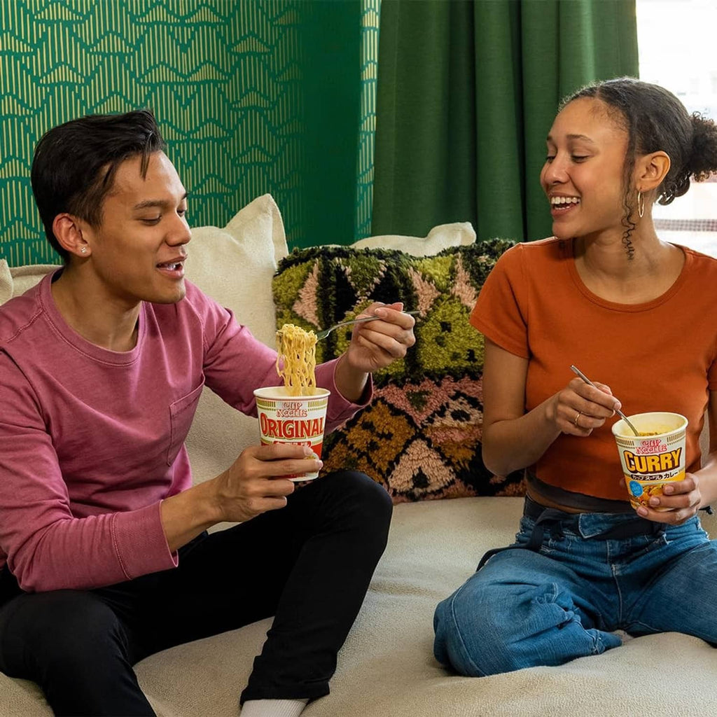 Two people holding curry cup noodles on couch, cups in hands