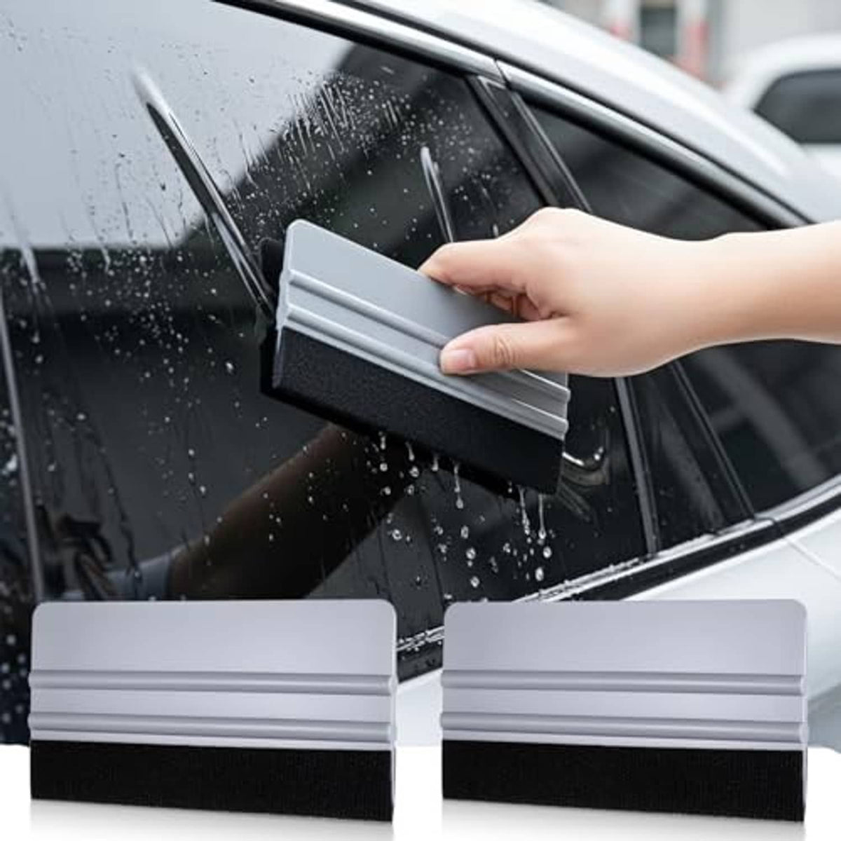 Gray plastic vinyl squeegee with black felt edge, held on a car window for tint film.