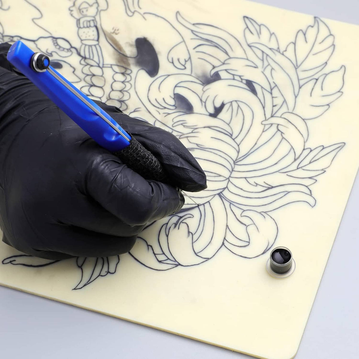 Tattoo poke-a-stick pen drawing stencil lines on stencil sheet with black-gloved hand