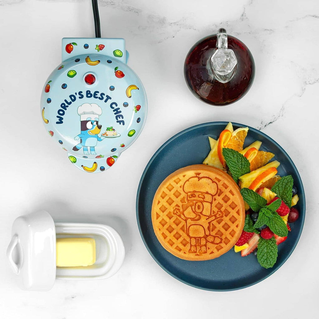 Light blue mini waffle maker with open lid; round waffle on plate with fruit