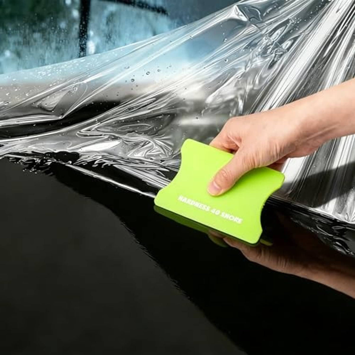 Lime green vinyl squeegee smoothing wet film on car surface, firm scraper