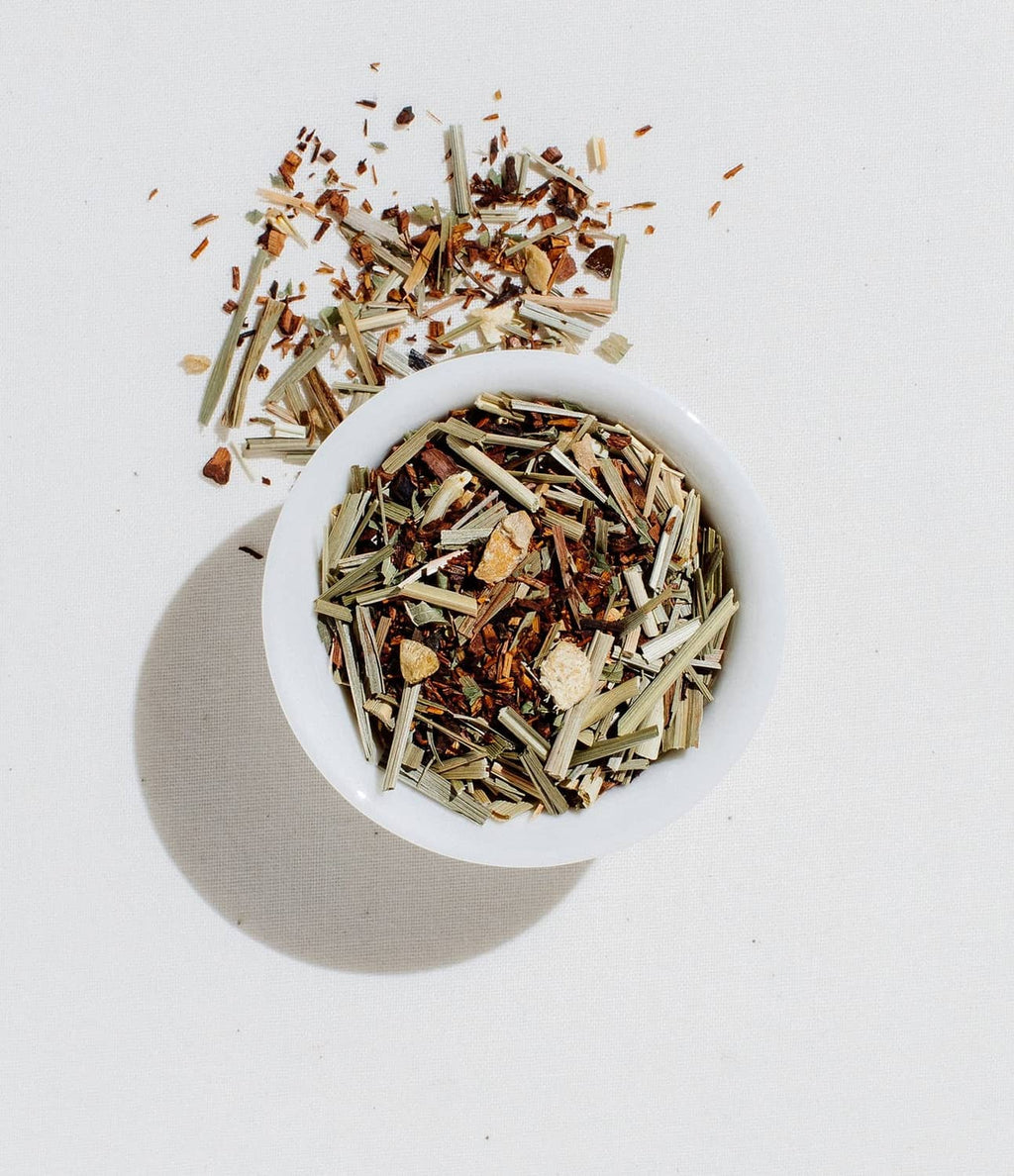 Loose leaf herbal tea blend in a white bowl with scattered leaf pieces