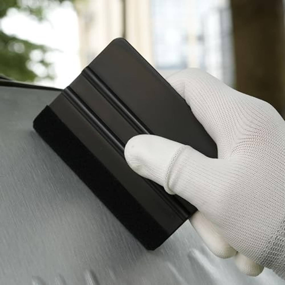 Black squeegee tool with felt edge, held by gloved hand on smooth surface