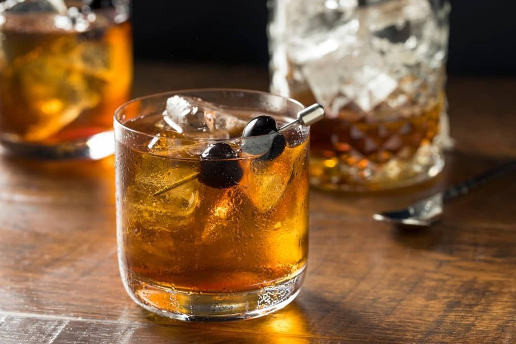 Clear tumbler with whiskey and ice, topped with dark maraschino cherries