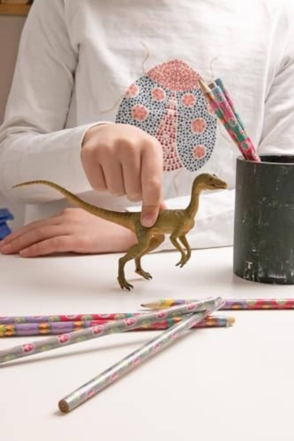 Compsognathus dinosaur figurine on a desk near drawing pencils and markers.