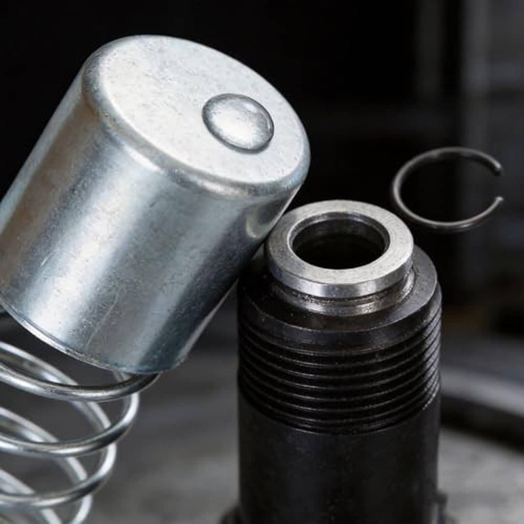 Hydraulic jack rebuild kit close-up: metal cap, threaded cylinder, and coil spring