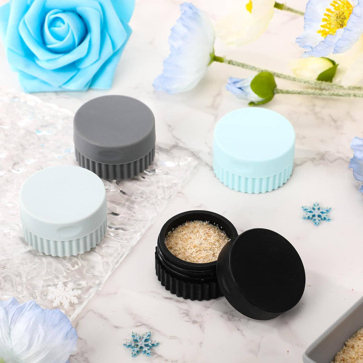 Set of silicone travel jars in grey and sky blue with lids, one open showing tan contents