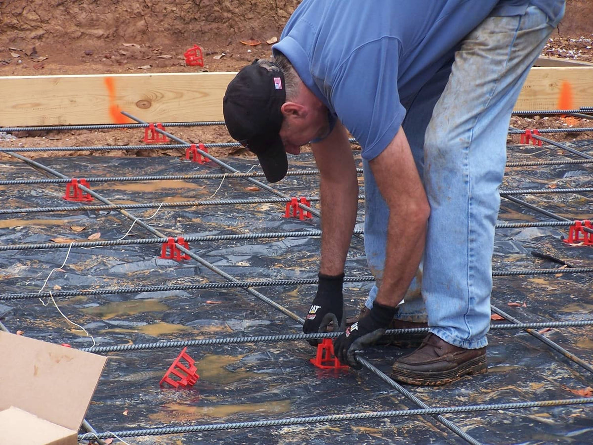 Red rebar chairs installed on a steel rebar mat by a worker