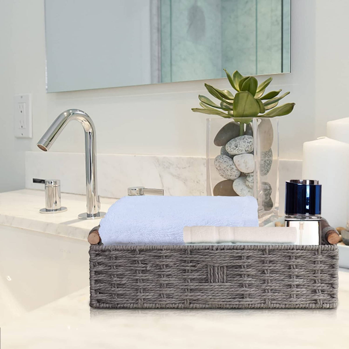 Grey woven storage basket on countertop with rolled white towels and wooden end handles.