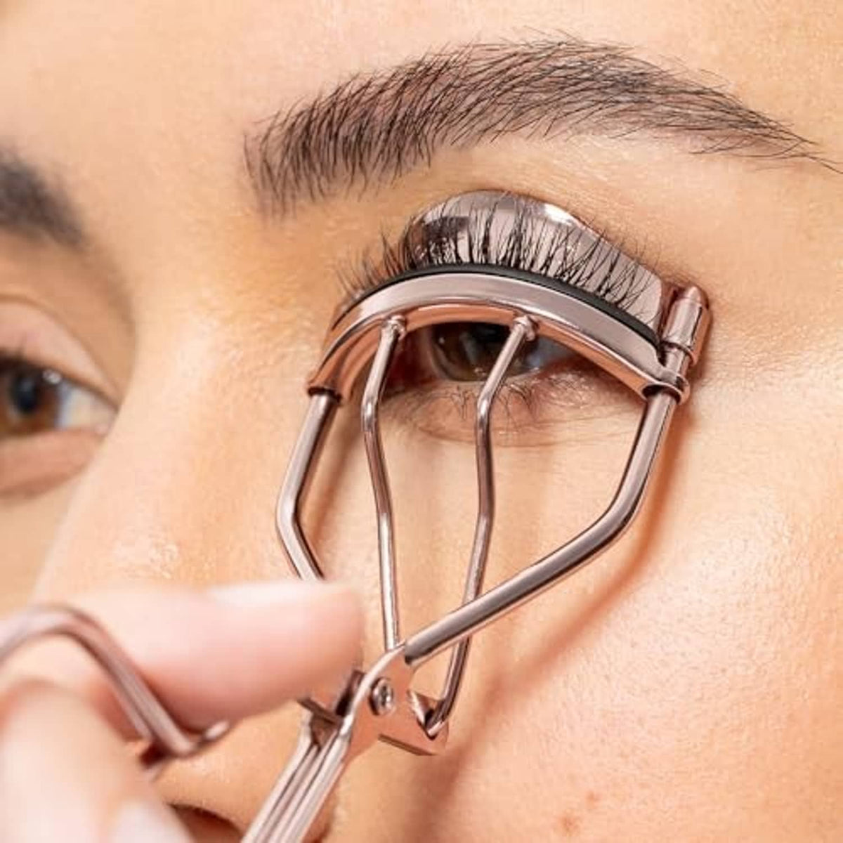 Rose gold eyelash curler clamping lashes near the eye