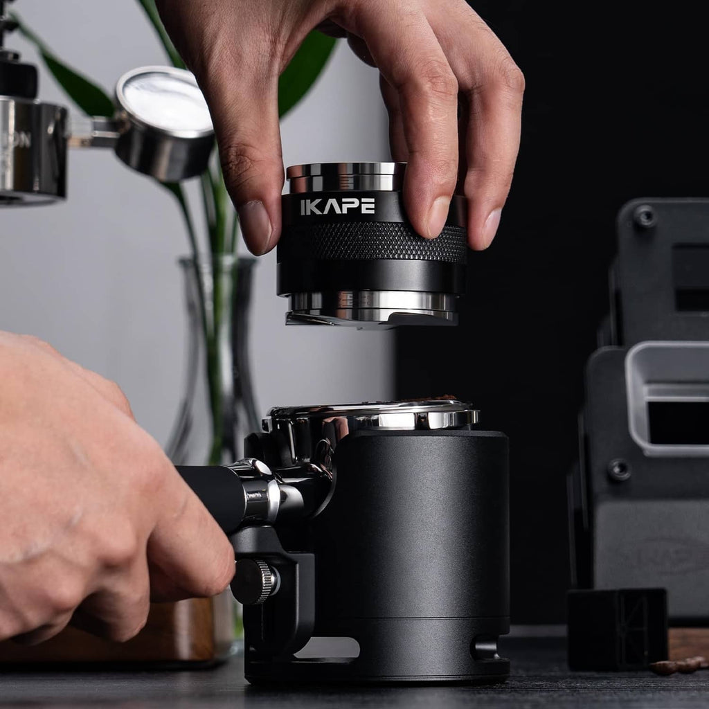 Hands placing a black espresso tamper onto the tool set station