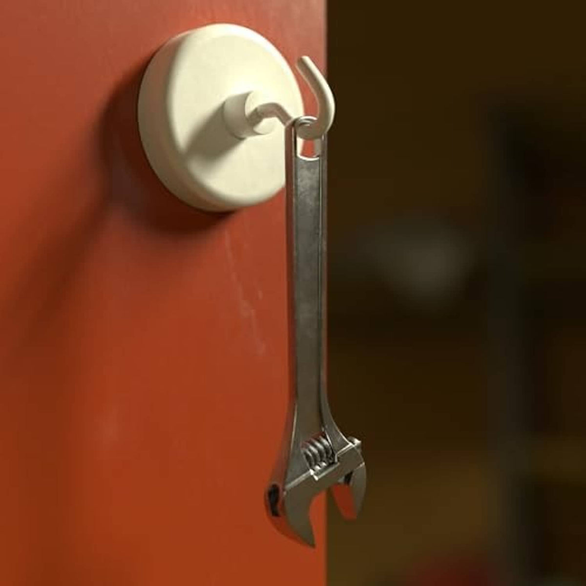 White magnetic hook holding a metal tool with prongs on a wall