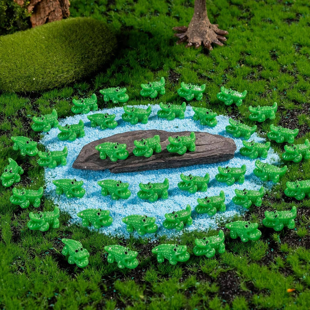 Mini green crocodile resin figurines arranged around a pond scene on blue gravel