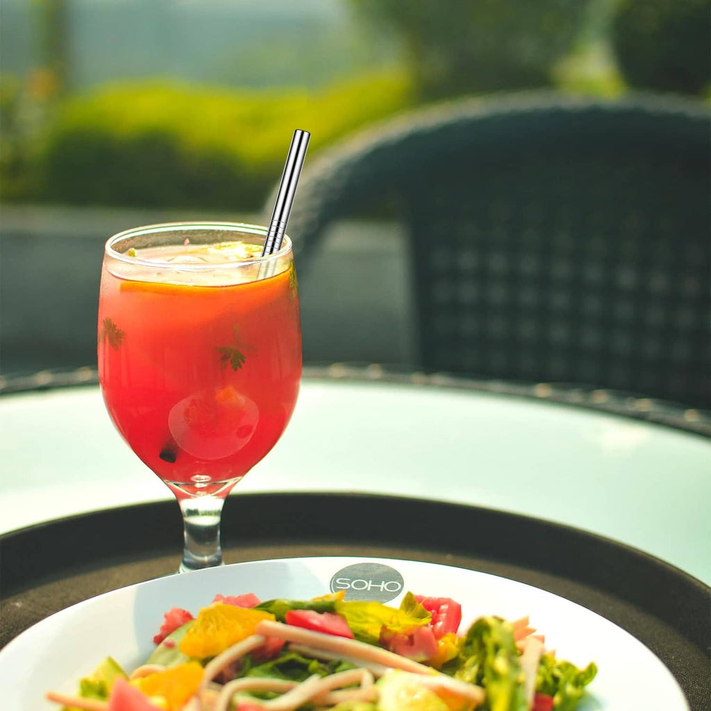 Metal cocktail straw standing in a glass of red drink, reusable sipping