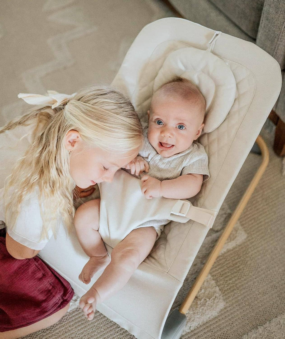 Beige baby bouncer seat with padded headrest and infant supported by caregiver