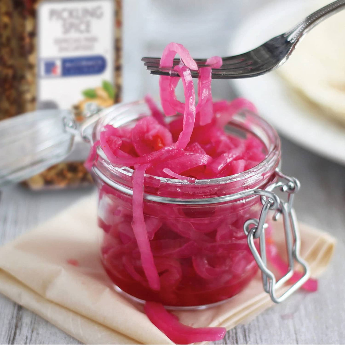 Small glass jar of pink pickled vegetables with a metal spoon and spice container