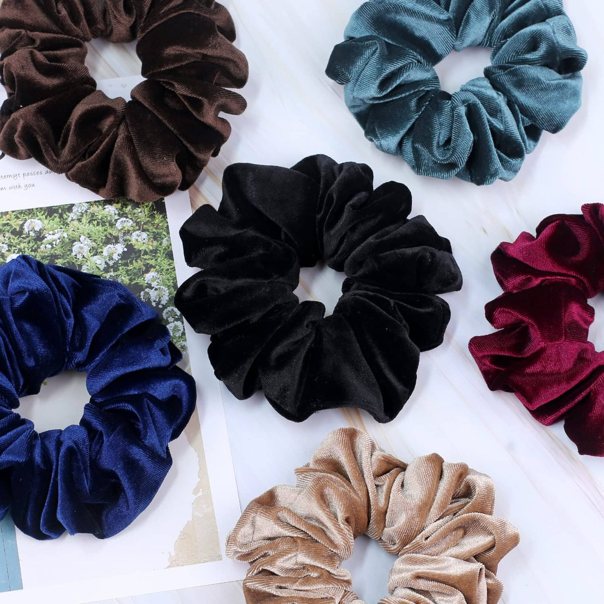 Assorted velvet scrunchies laid flat in black, navy, teal, brown, and burgundy