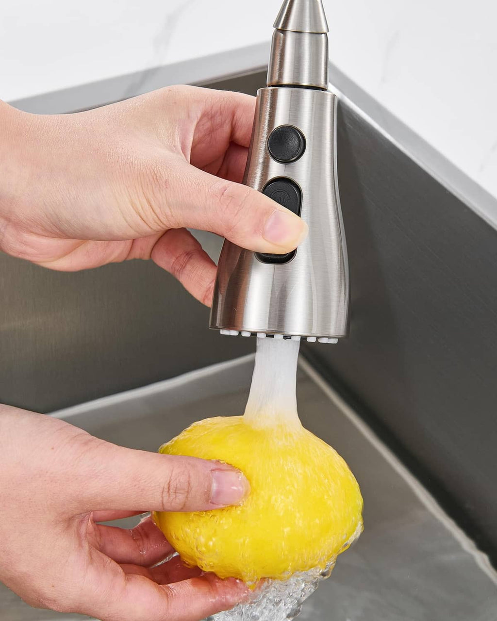 Hand holding brushed metal faucet sprayer head over sink with strong water flow
