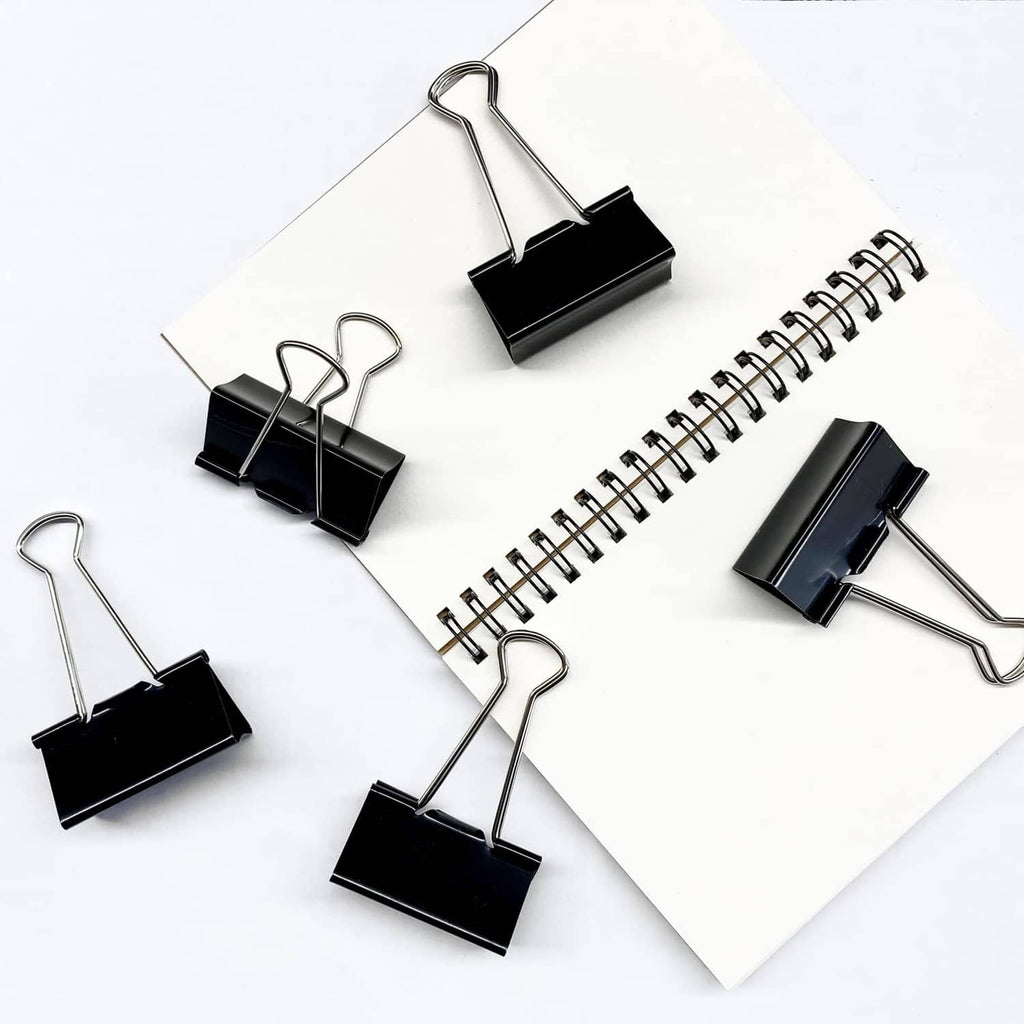 Multiple black binder clips with metal loops arranged on white papers