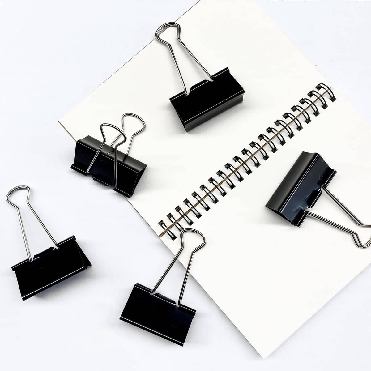 Multiple black binder clips with metal loops arranged on white papers