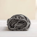 Gray linen fitted mattress cover, rolled bundle showing gathered elastic edge