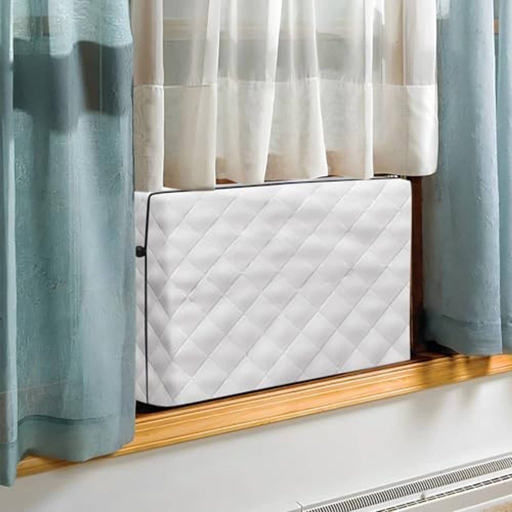Gray quilted indoor air conditioner cover fitted on a window unit beneath curtains.