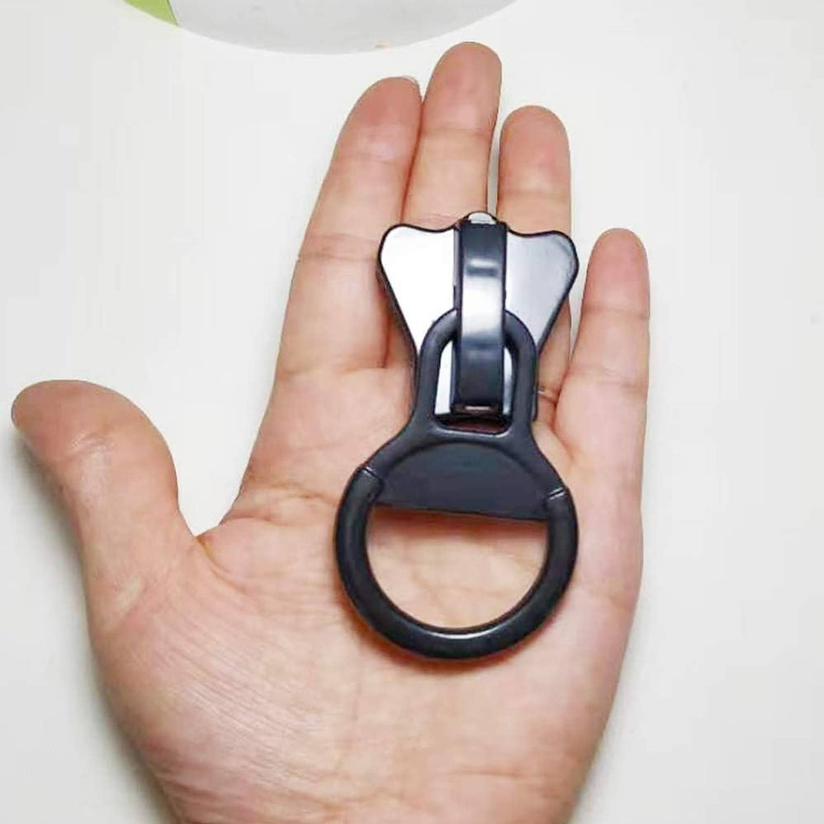 Black plastic zipper pull with ring handle held in an open hand.