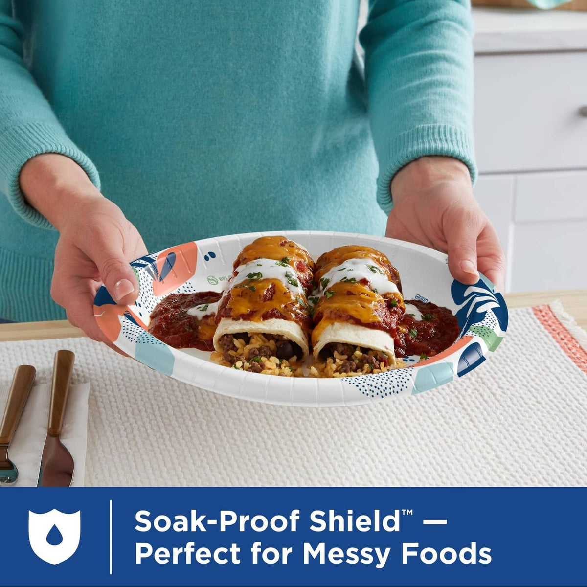 White paper plate with colorful rim pattern held by hands over food